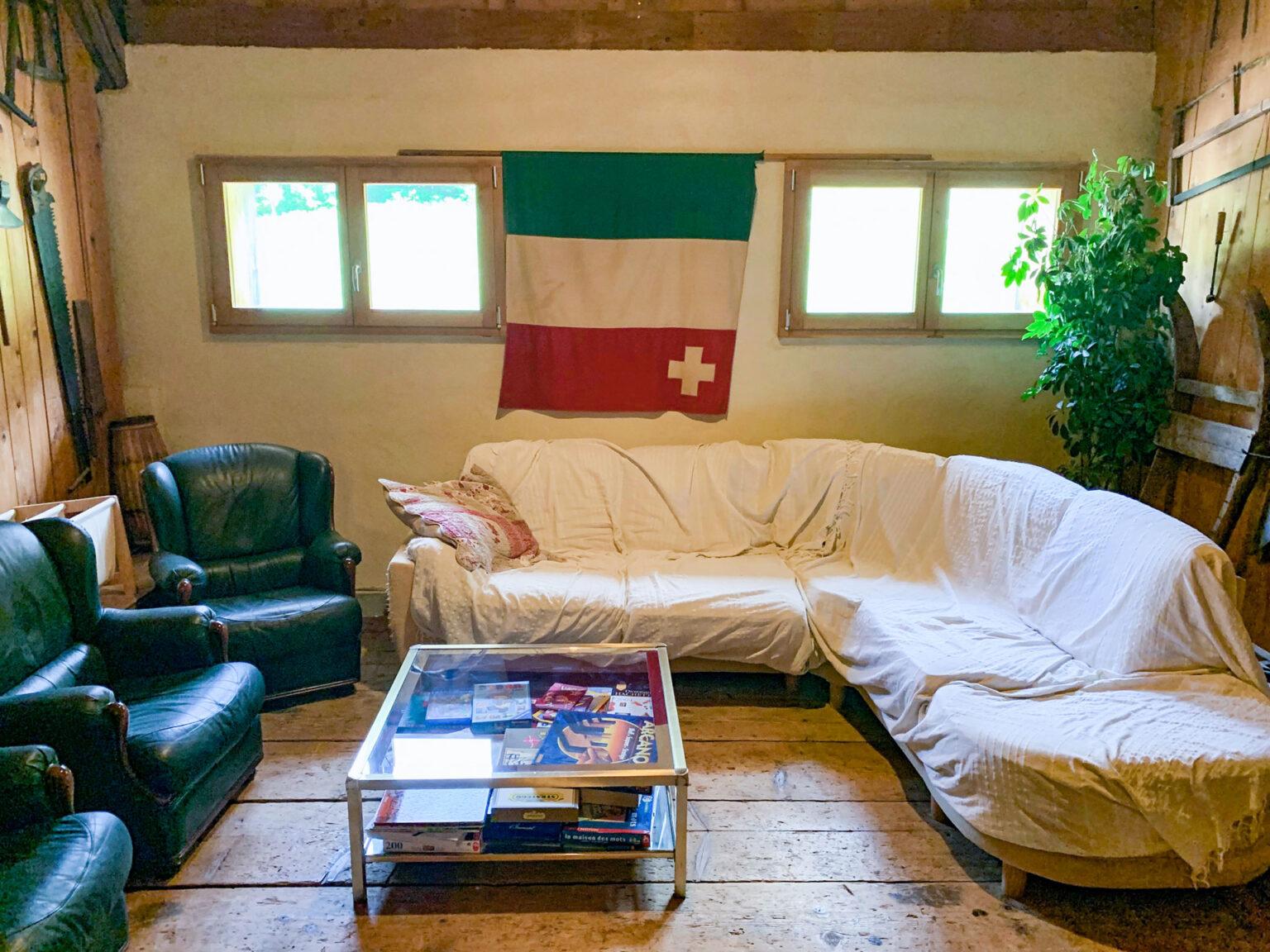 Au coeur des rêves au mont Chateleu salle de détente avec un canapé d'angle blanc sur la droite et trois fauteuils en cuirs vert sur la gauche, une table basse en verre contenant des jeux est au centre